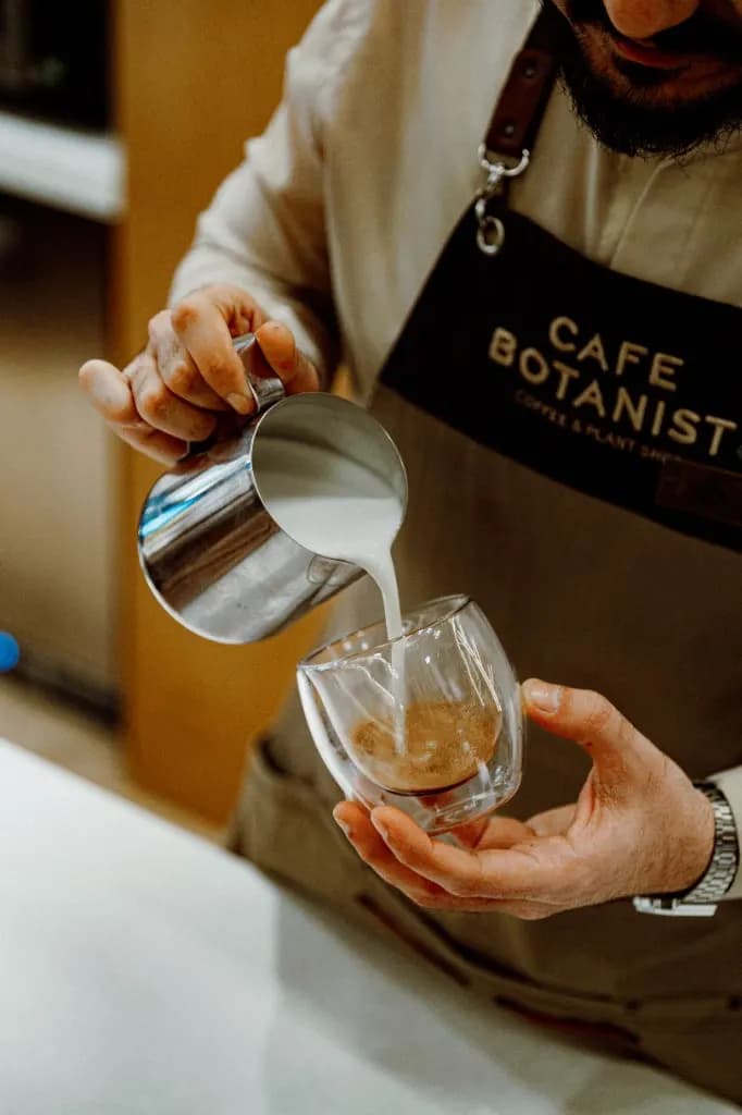 Barista gießt aufgeschäumte Milch in ein Glas